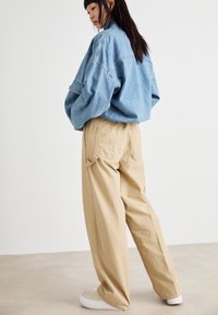 Veste en denim oversize bleu clair assortie à un pantalon large beige. Baskets à semelle épaisse. Look simple et décontracté.
