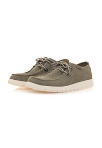 Zapatillas de lona verde oliva con suelas de goma blancas en contraste, que presentan cordones grises y acentos de cuero en el talón y en la marca lateral.