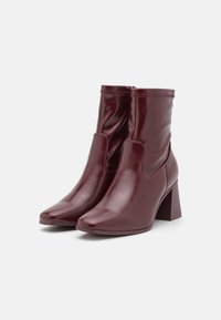 Bottines en cuir bordeaux à finition lisse, bout carré, découpe avant et talon épais. Elles disposent d'une fermeture éclair à l'arrière.