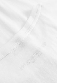 Witte katoenen T-shirt met een zachte textuur, voorzien van een subtiel reliëflogop in de rechterbenedenhoek en een ronde halslijn.