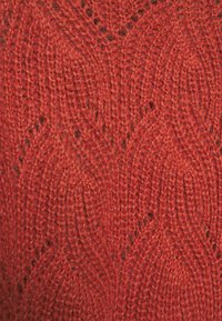 Strukturierter Strickstoff in lebhaftem Rot mit einem Blattmuster und offenen Maschen, der ein weiches, warmes, wollähnliches Material präsentiert.