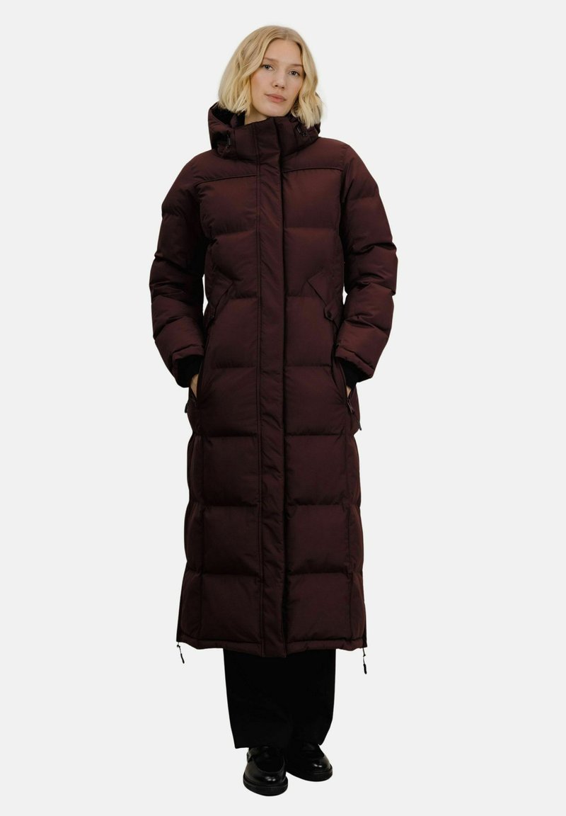 Lang dunjakke i mørk burgunder, med hette, quiltet tekstur, sidelommer og rett snitt, samt sort fottøy.