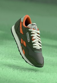 Zelené a oranžové tenisky Reebok vyrobené z semišových a textilních materiálů, s bílými tkaničkami a výrazným logem na boku a jazyku.