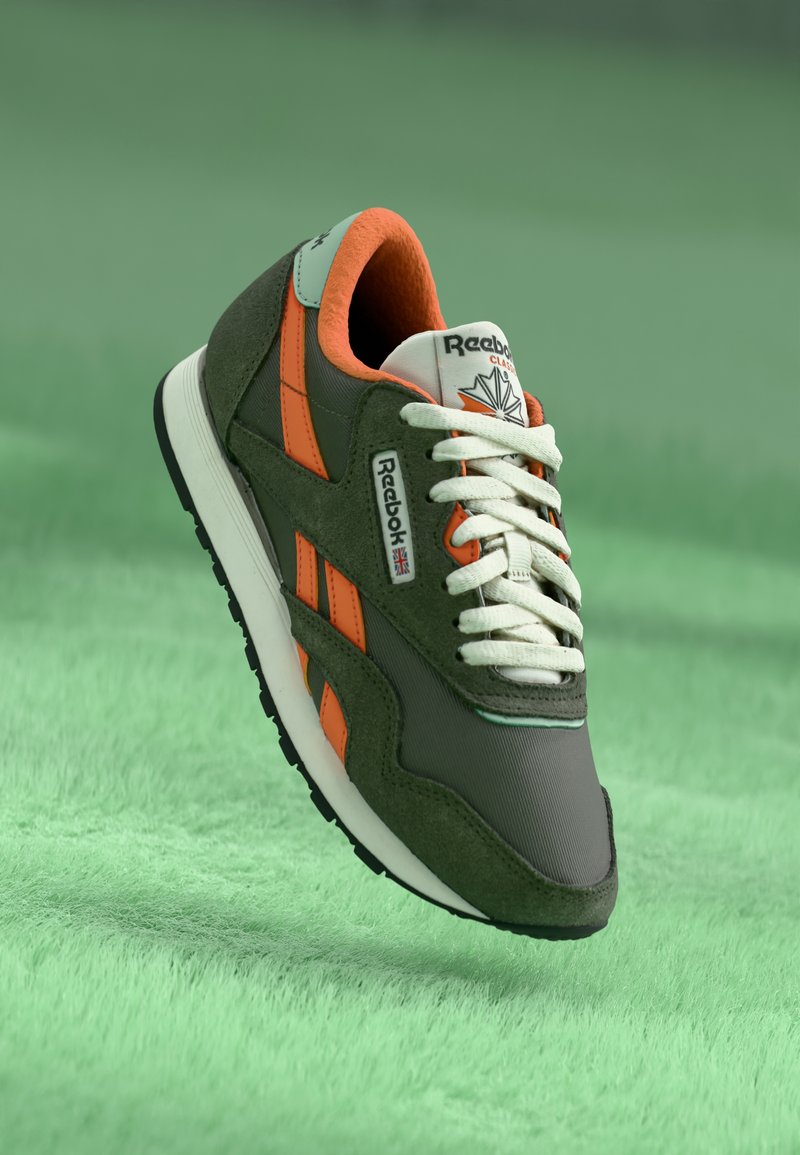 Zelené a oranžové tenisky Reebok vyrobené z semišových a textilních materiálů, s bílými tkaničkami a výrazným logem na boku a jazyku.