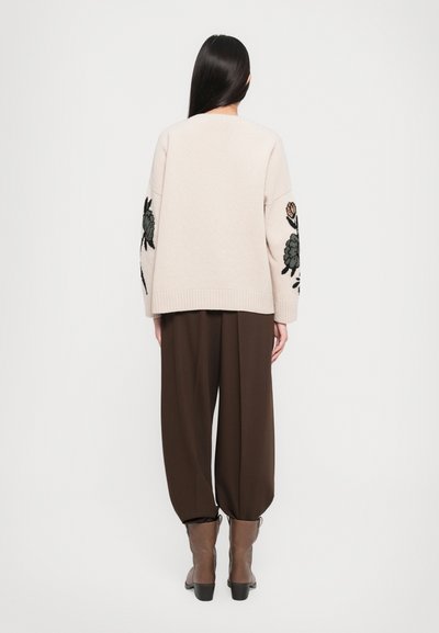 Beige trui met bloemenborduursel op de mouwen, in combinatie met bruine, losse broeken en bruine enkellaarsjes met een lage hak.