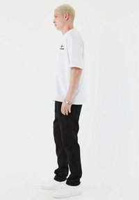 Hvid kortærmet t-shirt med sort grafik og logo, kombineret med sorte bukser og hvide sneakers. Enkelt, afslappet design og pasform.