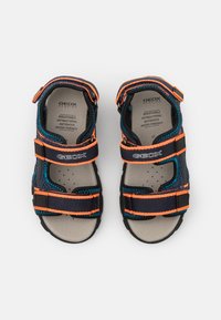 Sandalias azules y negras con detalles naranjas, que cuentan con correas ajustables, material transpirable, plantilla acolchada y suelas texturizadas.