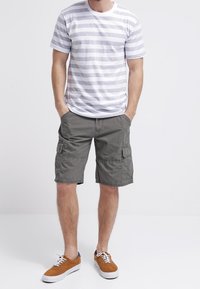 T-shirt a righe grigio e bianco, pantaloni cargo grigi con tasche laterali e sneakers basse marroni. Vestibilità casual e tessuto leggero.