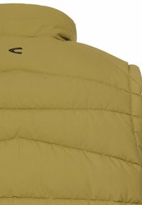 Olivgrüne Pufferjacke mit hohem Kragen, diagonaler Steppung und schwarzem Logo in der Nähe des Kragens. Glattes, strukturiertes Material.