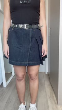 Jeans krilo s plisejsko zasnovo, temno modre barve in svetlim šivom. Kombinirano z črnim pasom z zaponkami v obliki srca.