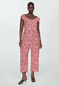 Červený a bílý květinový overal s volnými rukávy na ramena, zkrácenými širokými nohavicemi a přiléhavým korzetem, vyrobený z lehkého materiálu.