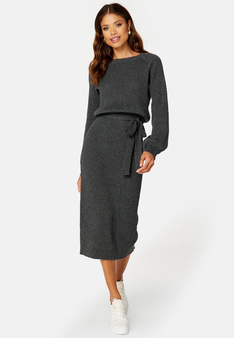 Graues Rippenstrickkleid mit langen Ärmeln, einer taillierten Silhouette und einem Bindegürtel. Kombiniert mit weißen Sneakers für einen lässigen Look.
