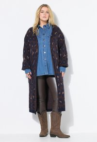 Cardigan long bleu marine avec imprimé léopard marron, superposé sur une chemise en denim et des leggings en cuir marron, associé avec des bottes de cowboy beiges.