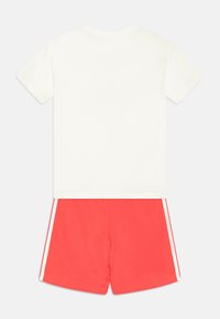 T-shirt bianca a maniche corte con dettagli rosa e pantaloni corti corallo con strisce laterali bianche, realizzati in morbido cotone.