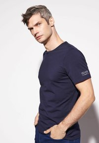 Granatowa, krótko rękawowa koszulka z gładkiego materiału, z okrągłym dekoltem i detalem logo na lewym rękawie.