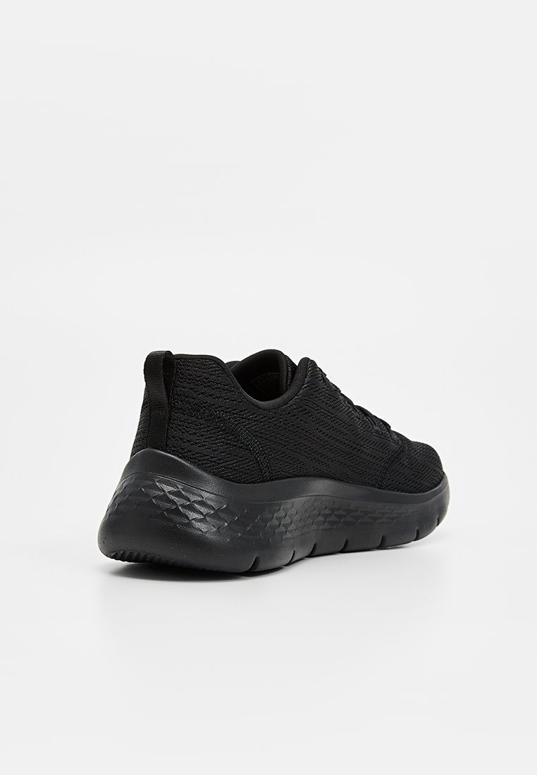 Zapatilla deportiva negra con un upper de punto texturizado, puntera redondeada y una suela de goma gruesa y acolchada con un patrón geométrico.