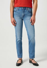 Vaqueros de mezclilla azul claro con corte recto, cintura alta, diseño clásico de cinco bolsillos y sutiles detalles de desgaste en la tela.