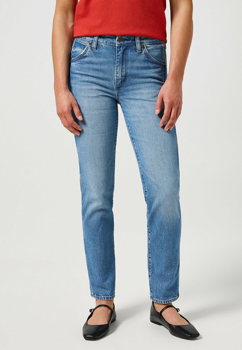 Vaqueros de mezclilla azul claro con corte recto, cintura alta, diseño clásico de cinco bolsillos y sutiles detalles de desgaste en la tela.