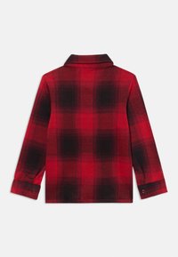 Κόκκινο και μαύρο καρό πουκάμισο, φτιαγμένο από μαλακό ύφασμα. Διαθέτει διπλωμένο γιακά και κουμπωτές μανσέτες. Η πίσω όψη δείχνει ένα καρό μοτίβο με διαφορετικές αποχρώσεις.