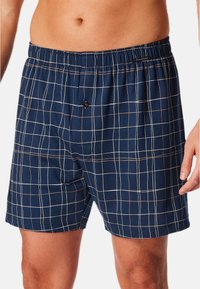 Boxers de algodón azul marino con un patrón de cuadrícula en blanco y marrón claro, que presentan una cinturilla elástica y un cierre con un solo botón.