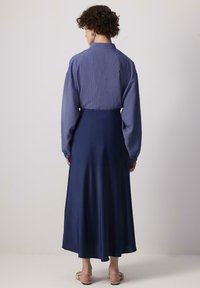 Chemise à manches longues rayée bleue avec un col montant, associée à une jupe longue en satin bleu marine uni. Comprend des poignets élastiques et des sandales plates.