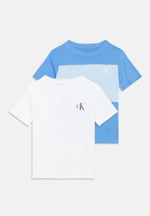 Deux t-shirts à manches courtes, l'un blanc uni avec un petit logo noir "cK", l'autre bleu avec une bande horizontale bleu clair et un logo "cK" blanc sur la poitrine.