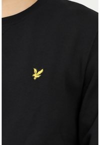 Felpa nera con collo rotondo, polsini a costine e un piccolo logo di un uccellino ricamato giallo sul petto. Tessuto morbido e strutturato.