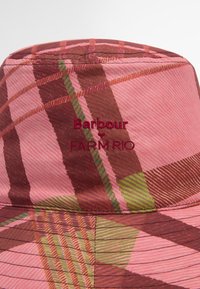 Chapéu bucket em padrão xadrez rosa com tons de castanho e verde. Apresenta detalhes de logotipo bordado e um acabamento em tecido texturizado.