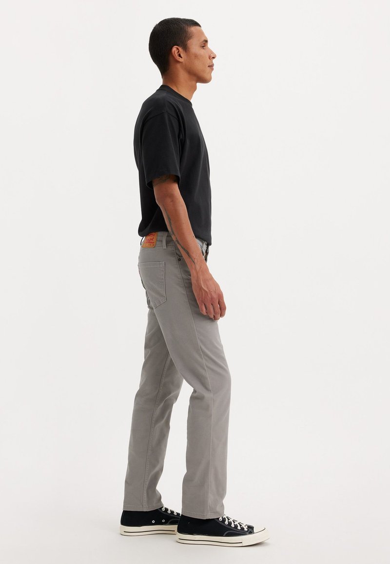 Jean gris avec une coupe droite, associé à un t-shirt noir à manches courtes et des baskets noires. Couture et poches visibles sur le jean.