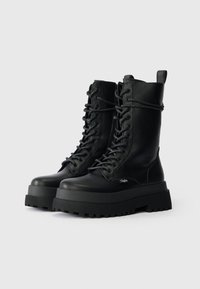 Melni ādas lace-up kaujas zābaki ar masīvu platformas zoli. Iespējas ietver teksturētu augšdaļu, biezi auklas un vilkšanas cilpu aizmugurē.