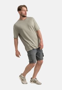 T-shirt grigio chiaro a maniche corte, abbinato a pantaloni cargo grigio scuro con tasche. Il modello indossa sneakers sportive di colore chiaro.