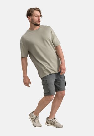 Lichtgrijze t-shirt met korte mouwen, gecombineerd met donkergrijze cargoshorts met zakken. Model draagt lichtgekleurde sport sneakers.