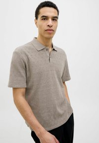 Lyhythihainen polo-paita vaaleanbeigessä värissä, jossa on teksturoitu kuvio, nappilista ja klassinen kaulus, valmistettu pehmeästä neuloskankaasta.