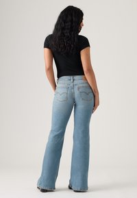 Svetlomodré zvonové rifle z denimu, s vysokým pásom, klasickými zadnými vreckami a viditeľnými detailmi švov. Hladká textúra, minimálne opotrebovanie.