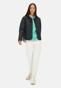 Vatteret sort jakke med knaplukning, båret over en grøn sweater og stribet skjorte. Sæt sammen med hvide bukser og grå sneakers.
