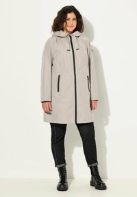 Jasnoszara wodoodporna kurtka z kapturem, z przodu na zamek błyskawiczny i dwiema bocznymi kieszeniami. Czarne akcenty przy zamku i zapięciach kieszeni.