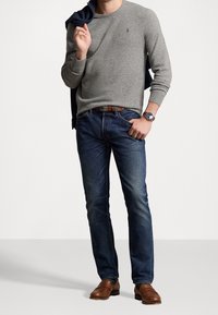 Pull gris, jean en denim bleu, chaussures en cuir marron. Le pull présente un col rond et un petit logo. Le jean est ajusté avec un léger effet délavé.