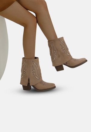 Stivaletti beige alla caviglia con punta leggermente affilata, caratterizzati da decorazioni ricamate a forma di ala e un tacco basso a blocco, realizzati in morbido camoscio.