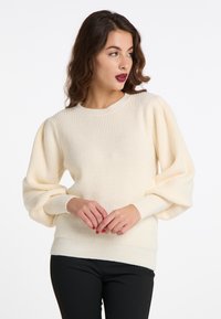 Pulover crem cu nervuri, cu mâneci tip balon și guler rotund. Material tricotat texturat conceput pentru a oferi căldură. Asortat cu pantaloni negri.