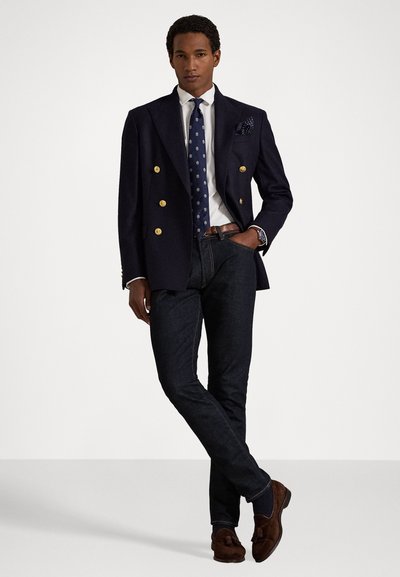 Μπλε ναυτικό σακάκι διπλής όψης με χρυσά κουμπιά, λευκό πουκάμισο, μοτίβο γραβάτας, σκούρα τζιν και καφέ σουέτ λόφερς. Καθαρός σχεδιασμός και εφαρμογή.