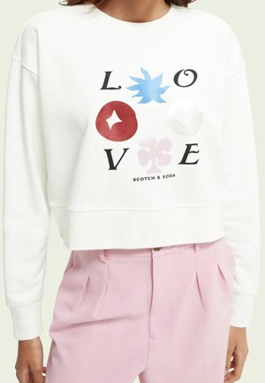 Sweatshirt blanc court avec un graphisme coloré portant le mot "LOVE" en noir, agrémenté de formes abstraites en bleu, rouge, rose et blanc.