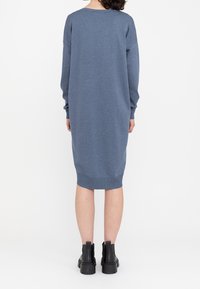 Abito felpa blu solido, tessuto a maglia, scollo rotondo, maniche lunghe, silhouette rilassata, orlo a coste, abbinato a stivali neri alla caviglia.