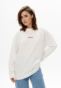 Weißes übergroßes Sweatshirt aus Baumwolle mit rundem Ausschnitt, versehen mit roter Stickerei mit dem Text "MIRONS" in der Mitte der Brust.