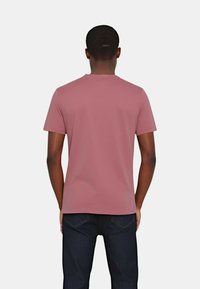 T-shirt a maniche corte di colore rosa tenue, realizzato in tessuto morbido. Presenta un classico collo tondo e una vestibilità rilassata, abbinato a jeans blu scuro.