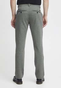 Pantalones gris texturizados con corte recto, dos bolsillos traseros con cierres de botón y calzado oscuro. La vista frontal no es visible.