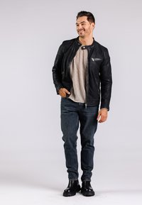 Chaqueta de cuero negra con bolsillos con cremallera, camiseta de punto gris claro, jeans azul oscuro y botas negras de tobillo. Material suave, diseño ajustado.