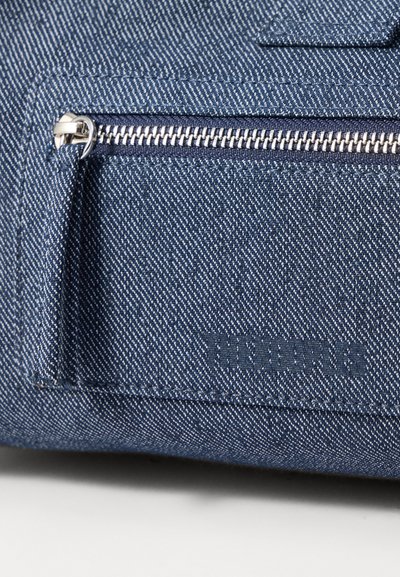 Τσάντα από τζιν με υφή μπλέ ύφασμα, ασημένιο φερμουάρ και ανάγλυφο λογότυπο. Περιλαμβάνει μια μικρή μπροστινή τσέπη με ασφαλές κλείσιμο με φερμουάρ.