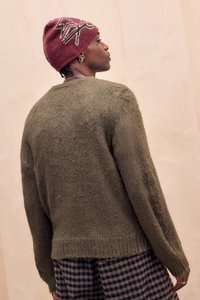 Olivengrøn, tekstureret sweater med lange ærmer, rund halsudskæring og ribbet kant, kombineret med et mønstret ternet skørt og en mørkerød beanie.