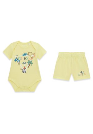 Ensemble pour bébé comprenant un body et un short jaunes avec un imprimé estival incluant un palmier, une glace, un soleil et le logo "GUESS".