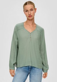 Groene blouse met lange mouwen en V-hals, geplooide schouderdetails en een dubbele knoopsluiting; textiele stof met een ontspannen pasvorm.